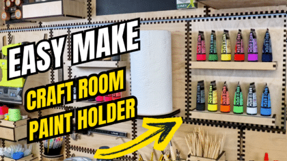 YouTube thumbnail showing a French cleat craft room wall with a paper towel holder and rainbow paint tube holder, overlaid with bold text “EASY MAKE CRAFT ROOM PAINT HOLDER” and a yellow arrow pointing at the paints.
