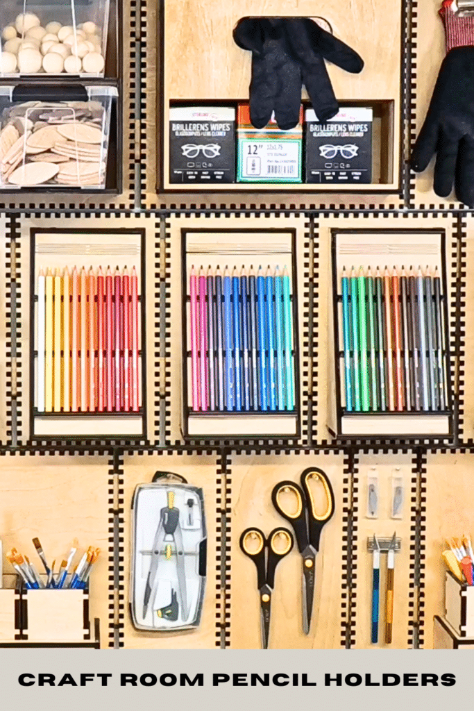 French cleat craft room wall with three colour‑sorted pencil holders, scissors and brushes neatly stored on plywood organizers, with the text “CRAFT ROOM PENCIL HOLDERS” at the bottom.