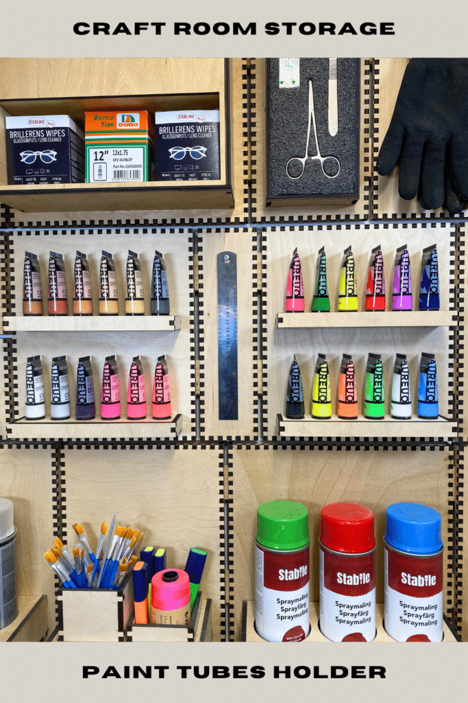 Craft room French cleat wall with a plywood paint tube holder storing two rainbow rows of paints between scissors, tools and spray cans, framed by text reading “Craft Room Storage – Paint Tubes Holder”.