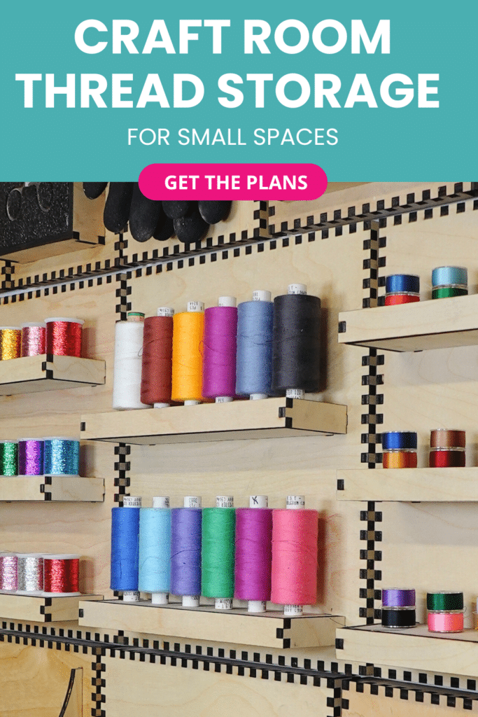 Laser‑cut plywood French cleat thread storage shelves on a craft room wall, holding neat rows of colourful thread spools in two shallow tiers with smaller bobbins on matching side shelves.