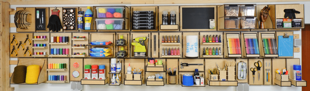 Full-width French cleat craft room wall with matching laser-cut plywood holders neatly storing yarn, paints, tools, brushes, paper towels, pencils and small supplies in organized rows.