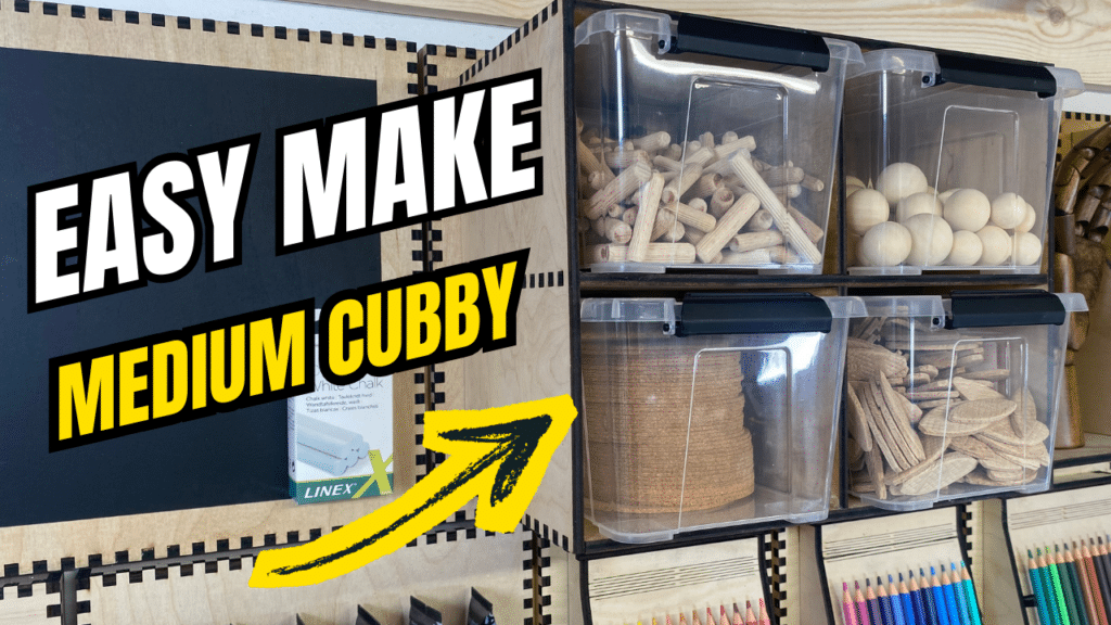 Laser-cut French cleat medium four-box cubby on a plywood wall, holding clear plastic bins filled with wooden dowels, spheres, and biscuits, with bold “Easy Make Medium Cubby” text and a yellow arrow overlay.