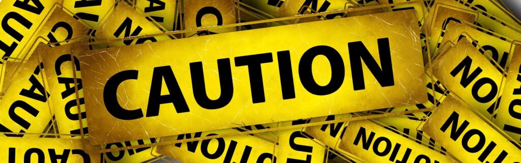 A collage banner of overlapping yellow warning signs with bold black text reading CAUTION. The signs are angled and have a distressed, weathered texture, providing a high-impact visual for workshop safety awareness and machine operation precautions.
