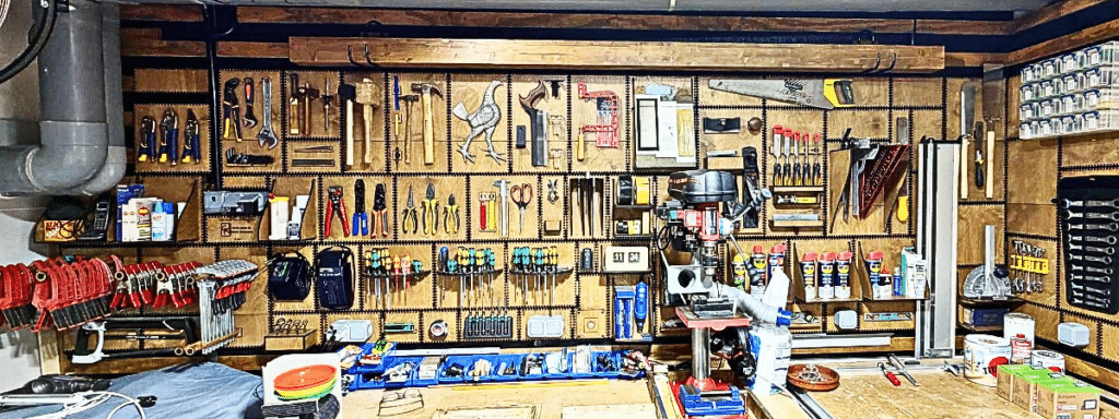 A full wall of Gavin's workshop organized edge-to-edge with French Cleat panels, holding dozens of hand tools, clamps, pliers, and hardware bins in neat rows, with a drill press and workbench below.