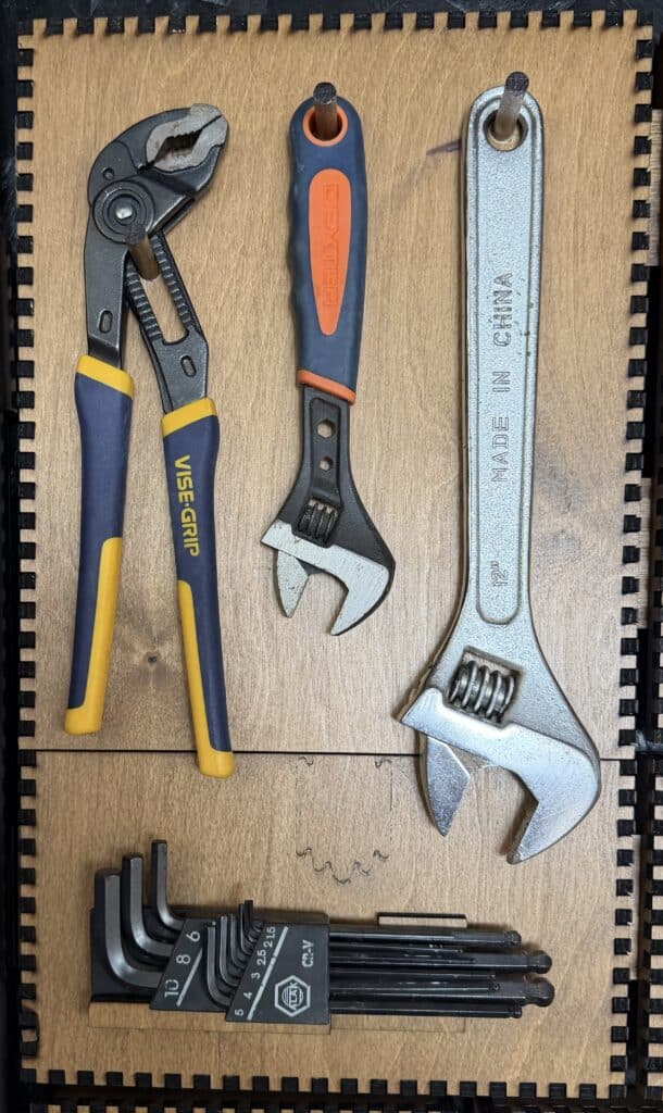 A Vise-Grip groove-joint plier, two adjustable wrenches, and a set of hex keys in a holder mounted on a French Cleat panel.