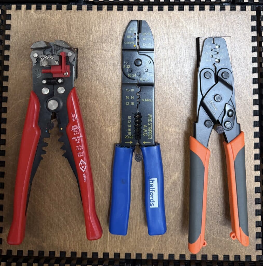 A red-handled automatic wire stripper, a blue-handled Halfords wire stripper, and an orange crimping tool mounted on a French Cleat panel.