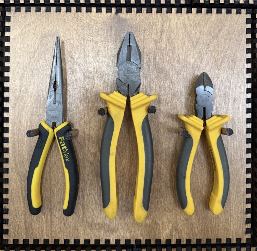 Three yellow-and-black Stanley FatMax pliers — long-nose, combination, and diagonal cutters — hanging on French Cleat pegs.