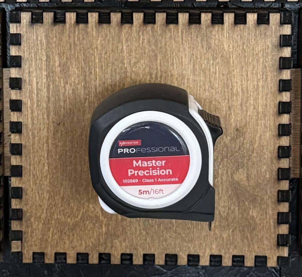 An Axminster Professional Master Precision tape measure held in a custom laser-cut wooden holder.