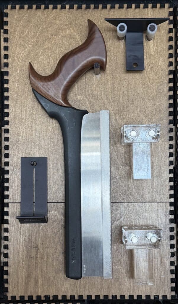 A wood-handled Japanese-style pull saw with a curved grip and small black metal jigs mounted on a French Cleat panel.