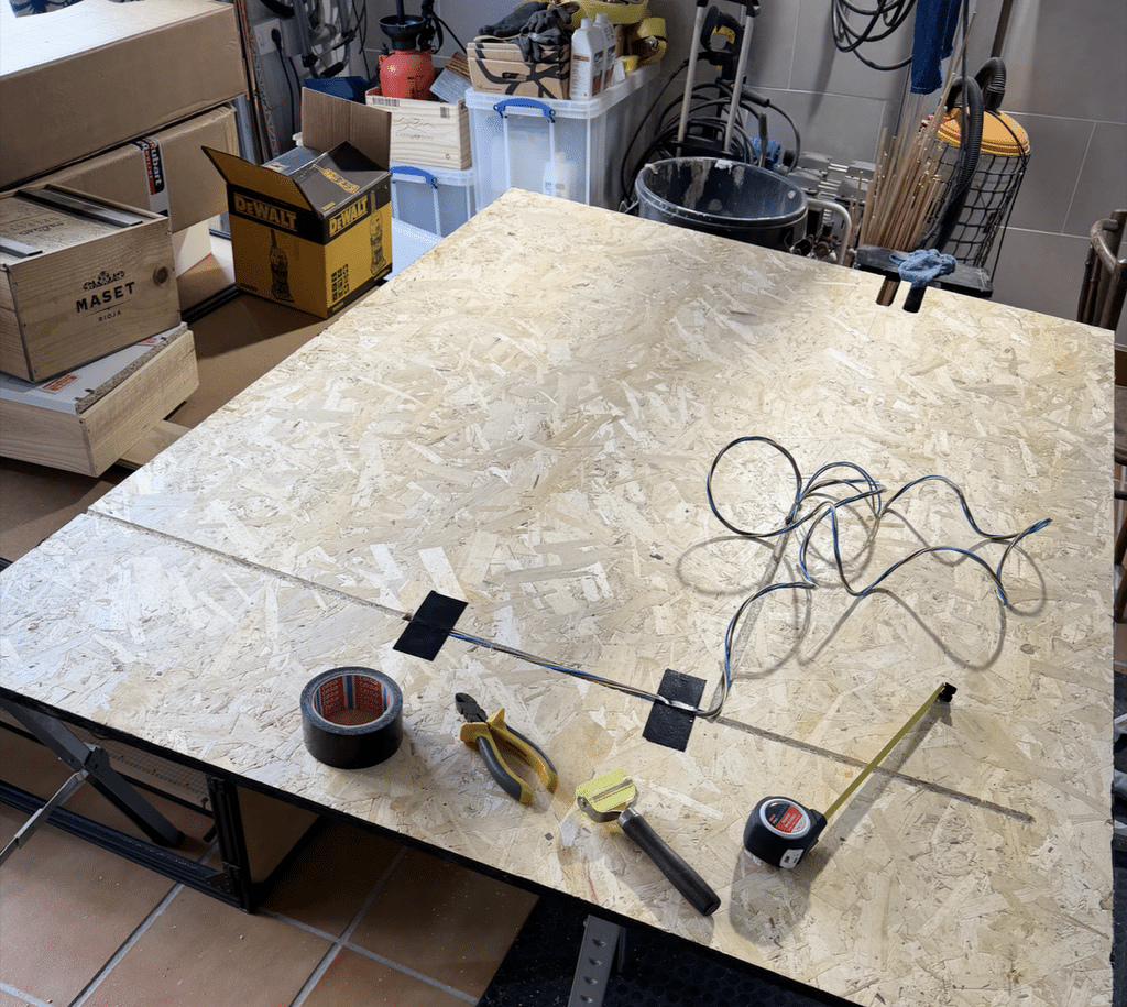 Gavin's OSB panel flipped to show routed channels cut into the back for hiding electrical wiring, letting him build outlets directly into the wall; both faces were varnished first to prevent warping, with the coiled cable, tape, and marking tools laid out on the bench.