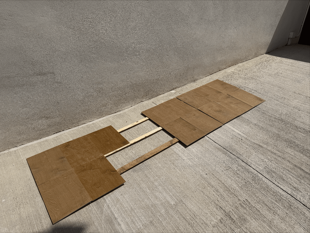 Cleat panels drying flat outdoors on the concrete, still separated with wooden spacers between the boards, catching the sun before they're mounted.