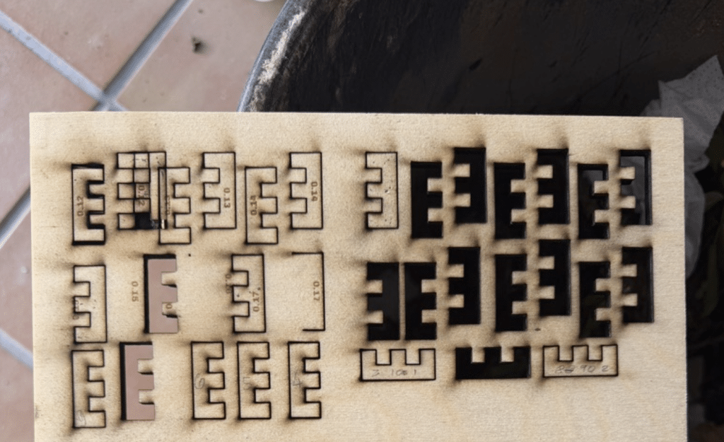 A test board of laser-cut cleat fingers at various kerf offsets, each labeled with its measurement, showing Gavin methodically dialing in the exact tolerance for a snug, interlocking fit.