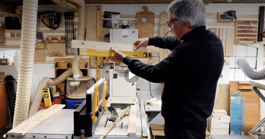 Woodworker checking a board with a spirit level in a workshop with French cleat tool storage on the wallLearn to build your French cleat wall